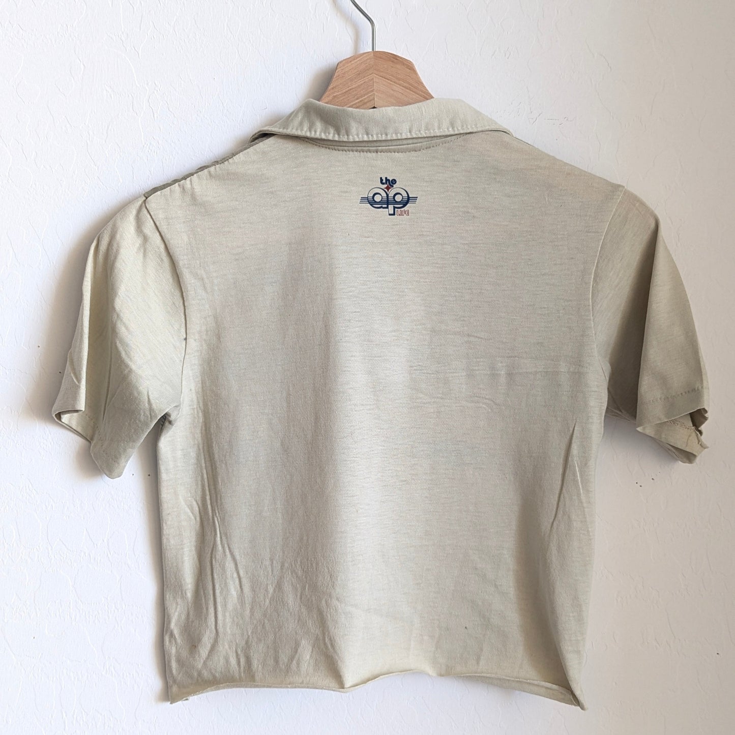 Light khaki polo shirt with a small logo on a hanger against a white background