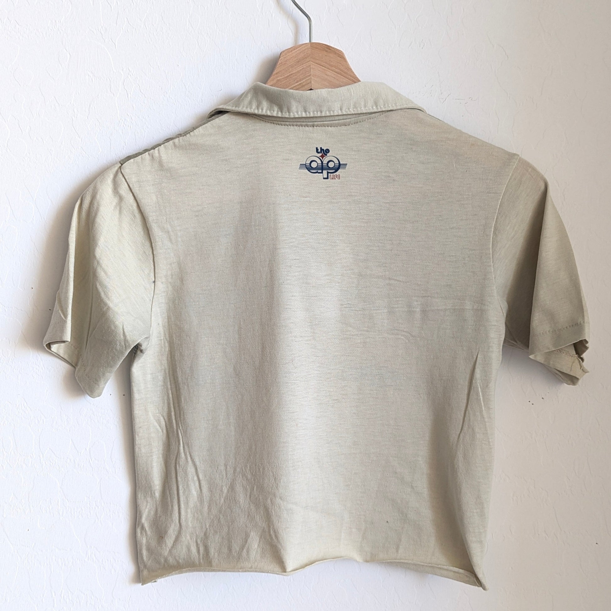 Light khaki polo shirt with a small logo on a hanger against a white background
