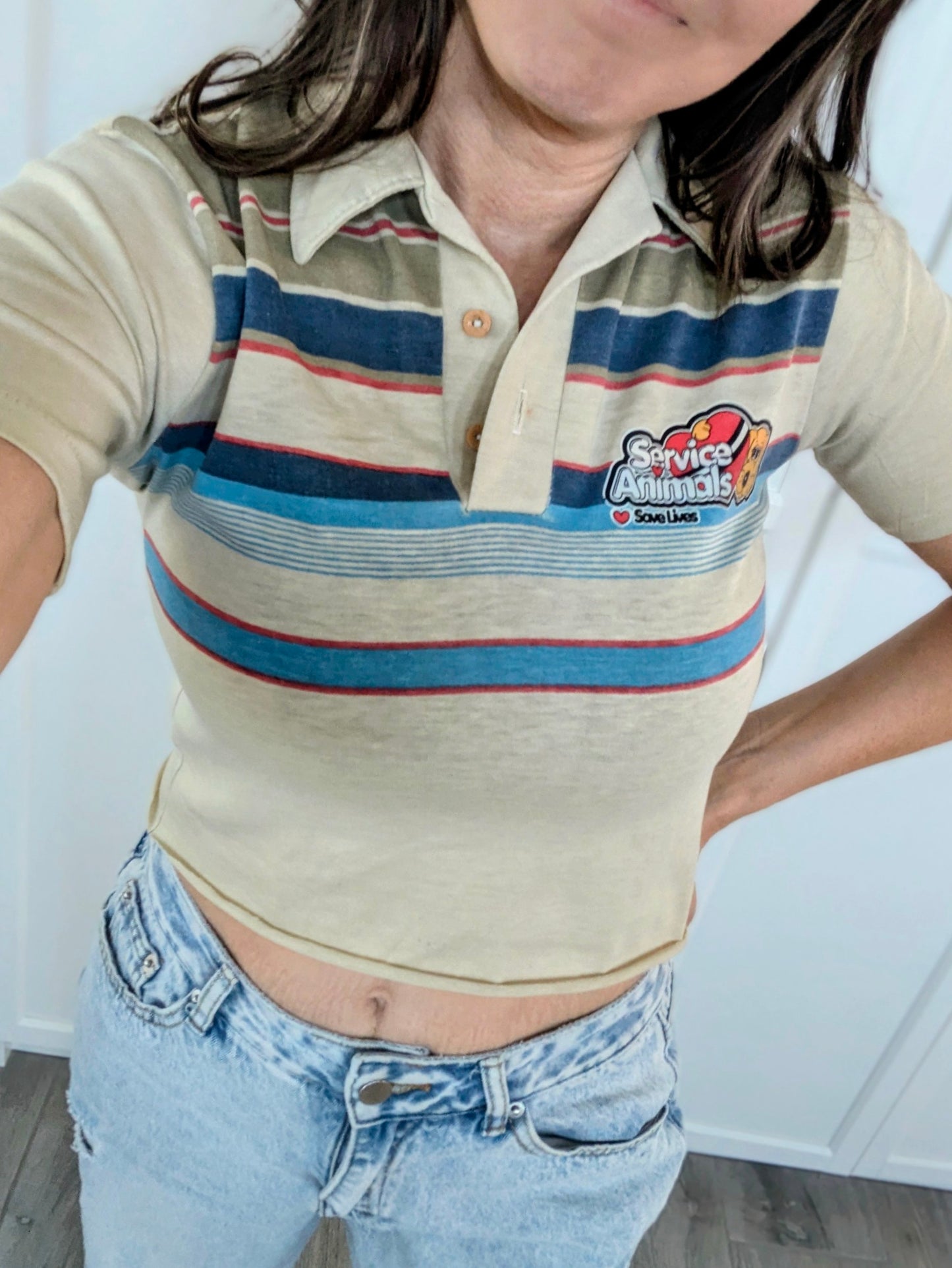 Person wearing a striped polo shirt with a logo and blue jeans indoors.