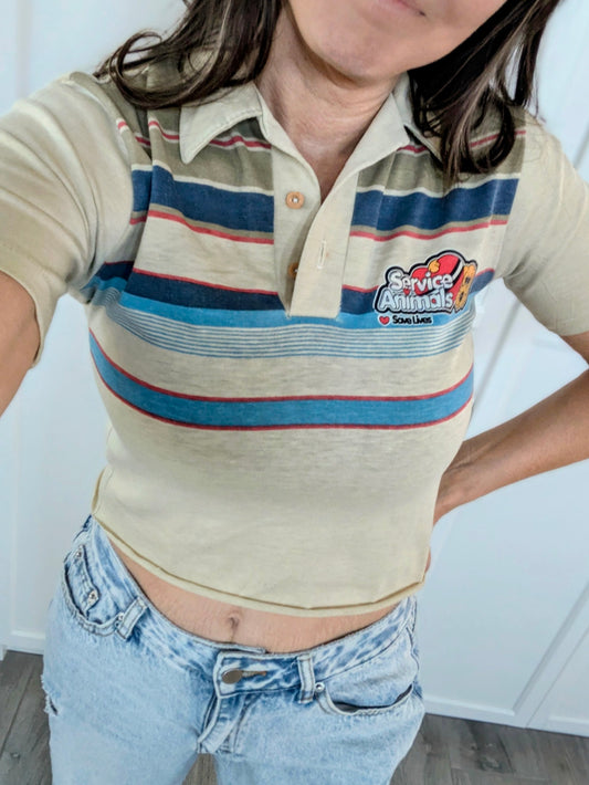 Person wearing a striped polo shirt with a logo and blue jeans indoors.
