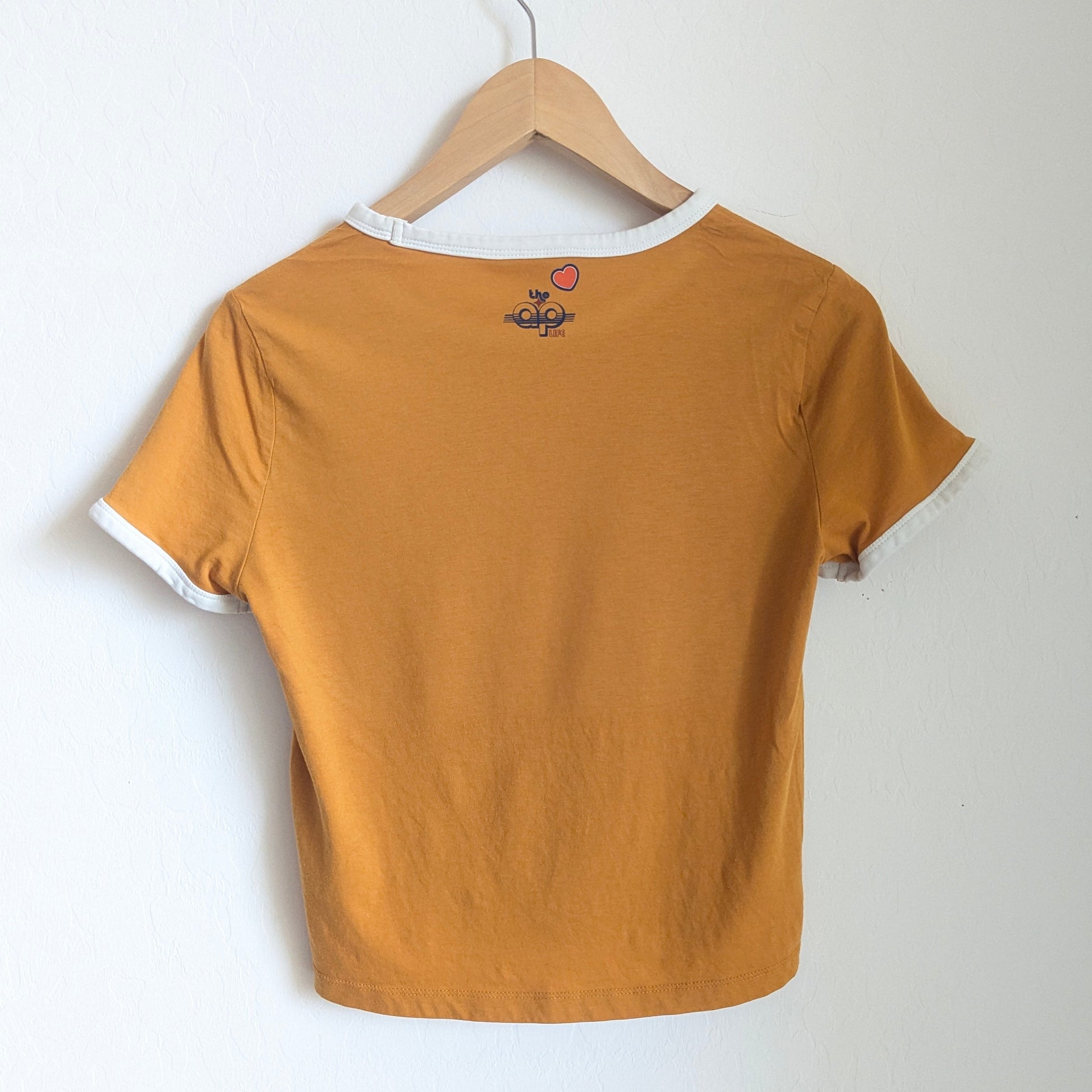 Mustard yellow t-shirt on a hanger against a white wall
